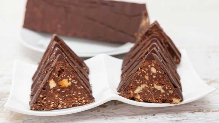 Dreiecksige St&uuml;cke von Schokolade liegen auf einem Teller, umgeben von einer gesamten Toblerone im Hintergrund.