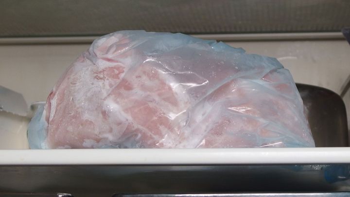 Eine gefrorene Fleischsorte befindet sich in einem durchsichtigen Beutel, eingelagert im K&uuml;hlschrank, um langsam aufzutauen.