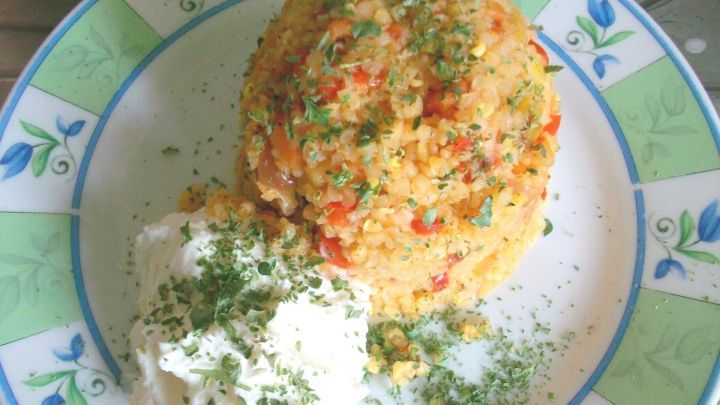 Ein schmackhafter Haufen Gem&uuml;se-Bulgur-Hanfsamen-Pfanne mit einer Portion cremigem Joghurt auf einem dekorativen Teller.