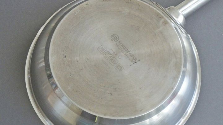 Ein gl&auml;nzender Pfannenboden wird gereinigt, um angebrannte Speisen zu verhindern. Der Hintergrund ist neutral grau.