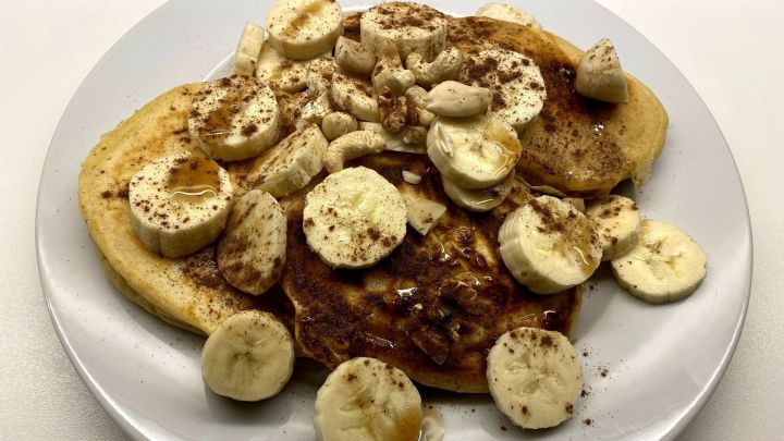 Auf einem wei&szlig;en Teller liegen amerikanische Buttermilch-Pancakes, garniert mit Bananenscheiben und Zimt.