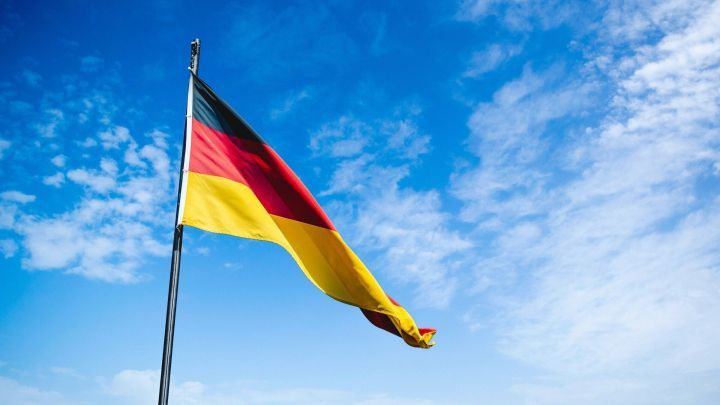 Eine Flagge mit den Farben Schwarz, Rot und Gold weht im Wind unter einem strahlend blauen Himmel.
