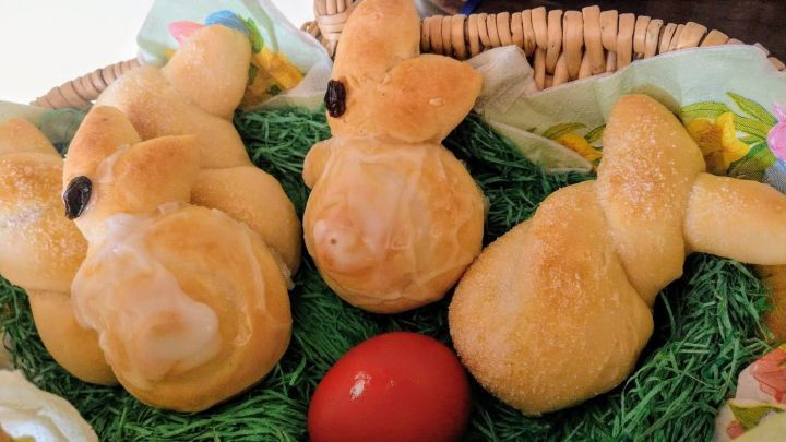 In einem Korb liegen mehrere gebackene Osterh&auml;schen aus Quark-&Ouml;l-Teig, umgeben von gr&uuml;nem Heu und einem roten Ei.