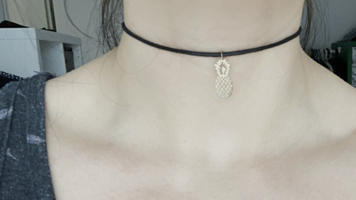 Ein Choker-Halsschmuck mit einer kleinen Ananas-Edelstahlanh&auml;nger wird an einem Hals getragen, der leicht sichtbar ist.
