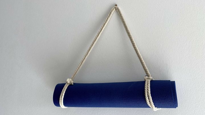 Eine blaue Yogamatte ist mit einem Seil aufgeh&auml;ngt, das sie sicher zusammenh&auml;lt, vor einer hellen Wand.