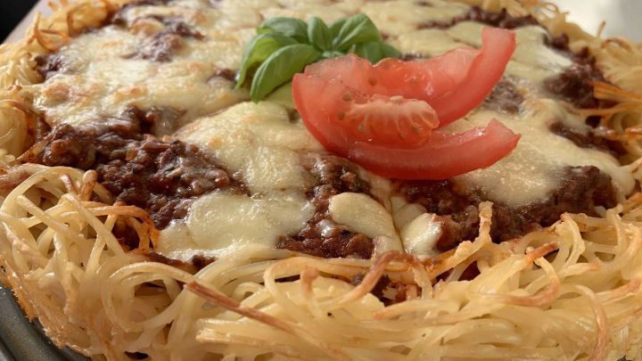 Eine appetitliche Spaghetti-Bolognese-Torte zeigt einen goldbraun gebackenen Nudelteig, garniert mit K&auml;se, Tomate und Basilikum.