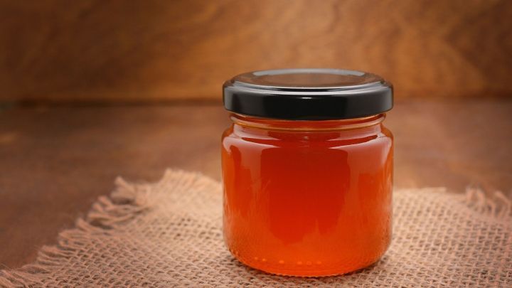 Ein Glas Honig steht auf einem gewebten Untergrund und f&auml;ngt das Licht ein, was die goldene Farbe des Honigs betont.