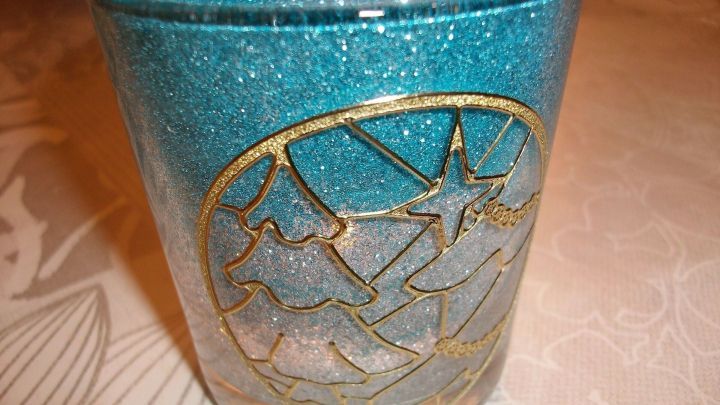 Ein glitzerndes Teelichtglas in Blau, verziert mit goldenen Motiven, steht auf einem neutralen Tischmuster.