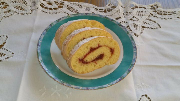 Auf einem Teller liegen einige Scheiben einer Biskuitrolle, die mit Puderzucker bestreut und mit Fruchtf&uuml;llung gef&uuml;llt sind.