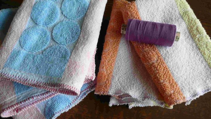 Bunte Frottee-Handt&uuml;cher liegen auf einem Tisch, w&auml;hrend eine lila N&auml;hgarnrolle daneben darauf wartet, verwendet zu werden.