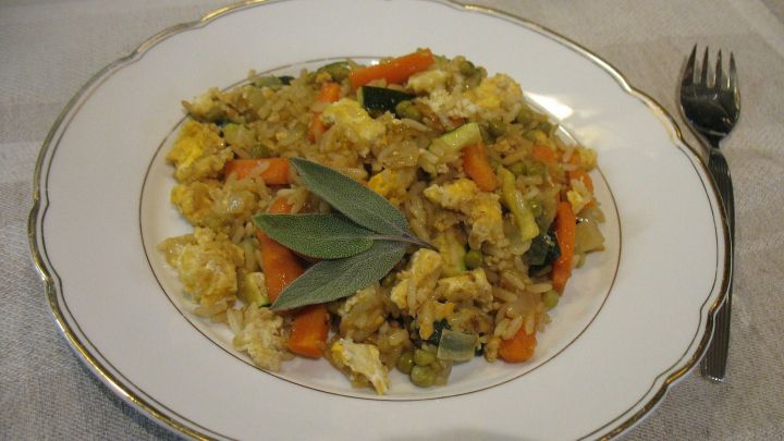 Ein Teller Bratreis mit Gem&uuml;se und Ei, garniert mit frischen Salbeibl&auml;ttern, auf einem eleganten Tisch.