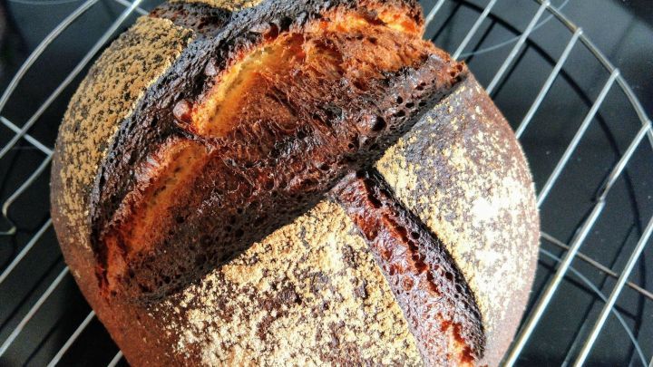Ein frisch gebackenes Dinkel-Sauerteigbrot liegt auf einem Kuchengitter, w&auml;hrend es abk&uuml;hlt und seine knusprige Kruste zeigt.
