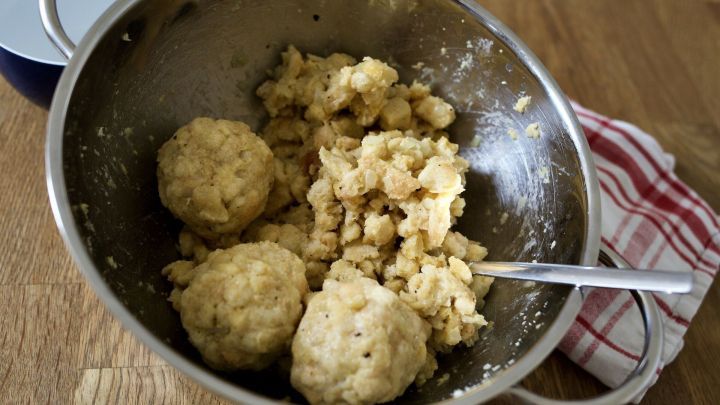 Kleine Teigb&auml;llchen, bereit zum Kochen, liegen in einer Sch&uuml;ssel, umgeben von br&ouml;seligem Teig auf einem Holztisch.