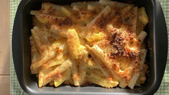 Ein goldbraun &uuml;berbackener Spargel mit Kartoffeln liegt in einer schwarzen Auflaufform auf einem karierten Tischdeckchen.