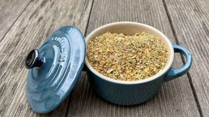 Ein t&uuml;rkisfarbener Topf steht offen auf einem Holztisch und enth&auml;lt trockenes Gem&uuml;sebr&uuml;he-Pulver, w&uuml;rziger Mix.