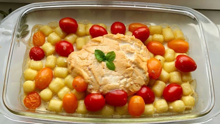 Ein Gnocchi-Miree-Auflauf liegt in einer Auflaufform, umgeben von bunten Tomaten und Gnocchi auf einem Fensterbrett.