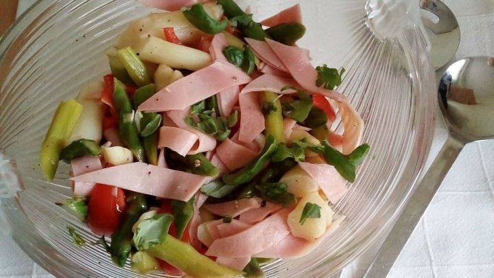 Ein bunter Spargel-Salat mit Schinken, frisch angerichtet in einer Glas-Sch&uuml;ssel, steht auf einem wei&szlig;en Tuch.