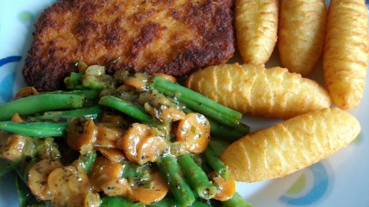 Auf dem Teller liegt gebratenes Fleisch neben Karotten-Bohnen-Gem&uuml;se und knusprigen Kartoffelbrei-St&uuml;ckchen.