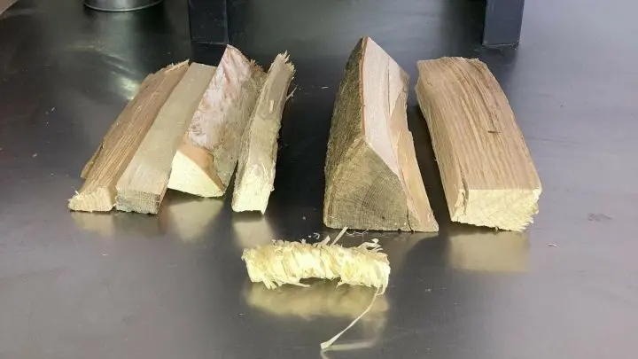 1 viereckiges Holzstück, 1 dreieckiges Holzstück, 4 Anzündehölzer,1 Anzünder. Viereckiges Holz quer einlegen (hinten). Vorne quer das dreieckige Holz. Kleinen Zwischenraum lassen. Zwischen rein wird der Anzünder gelegt.
