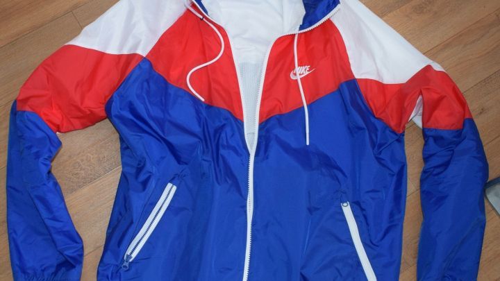 Eine bunte Nike-Jacke liegt flach auf einem Holzfu&szlig;boden, bereit zum Spenden oder f&uuml;r die Entsorgung von Altkleidern.