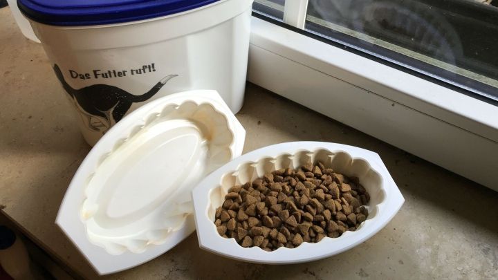 Ein Futternapf aus Recycling-Schalen steht mit Katzenfutter gef&uuml;llt auf einer Fensterbank neben einem Eimer.