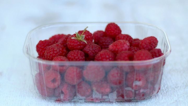 Frische Himbeeren in einer durchsichtigen Verpackung liegen auf einem hellen, strukturierten Untergrund, bereit zum Verschenken.