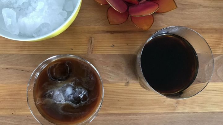 Ein Glas vietnamesischer Kaffee mit Eisw&uuml;rfeln neben einer Sch&uuml;ssel mit crushed ice und einer dekorativen Blume auf Holz.