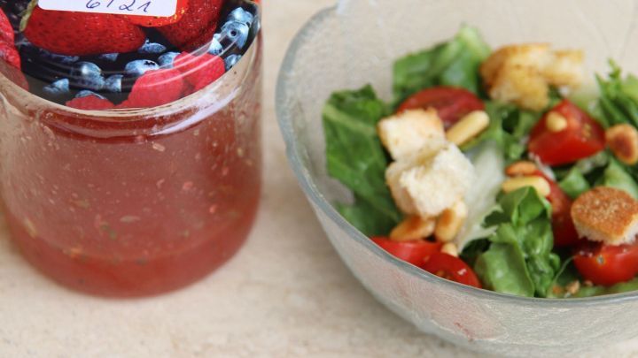 Ein Glas Marmelade steht neben einem frischen Salat mit Tomaten, Croutons und Pinienkernen, bereit zum Servieren.