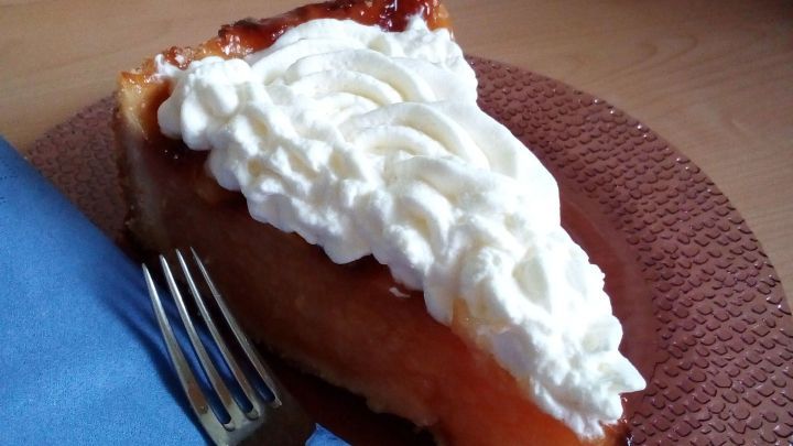 Eine saftige Apfeltorte liegt auf einem braunen Teller, dekoriert mit Sahne, neben einer blauen Serviette und einer Gabel.