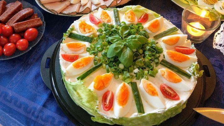 Eine Salattorte besteht aus frischem Gem&uuml;se, dekorativ angeordnet und serviert auf einem eleganten Tisch mit weiteren Speisen.