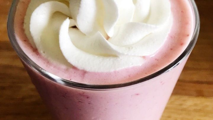 Ein Erdbeer-Bananen-Milchshake in einem Glas, garniert mit Sahne, steht auf einem Holztisch.