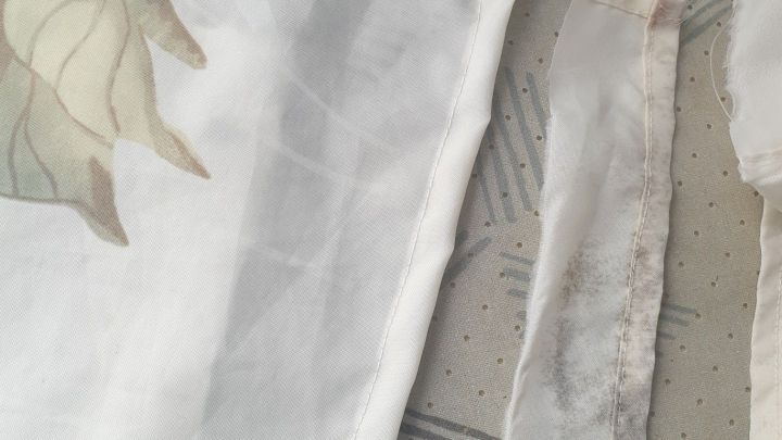 Ein Duschvorhang mit Schimmel am Saum liegt auf einer gemusterten Oberfl&auml;che, w&auml;hrend er leicht gefaltet ist.