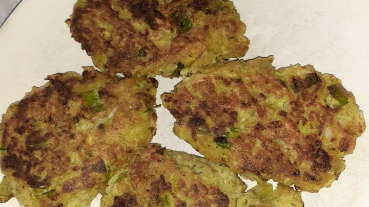 Krosse Brokkoli-Frikadellen liegen auf einem wei&szlig;en Teller, umgeben von einem schlichten Tisch mit Textil.