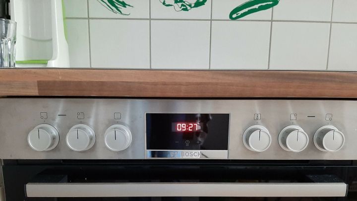 Ein Herd mit sechs hervorgehobenen Kn&ouml;pfen zeigt die Zeit von 09:27 an, umgeben von einer modernen K&uuml;che.