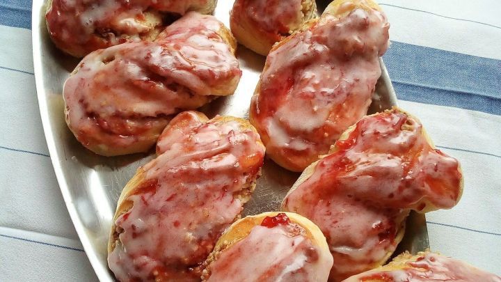 Hefeschleifen mit einer gl&auml;nzenden Glasur liegen auf einer silbernen Platte, umgeben von einem gestreiften Tischtuch.