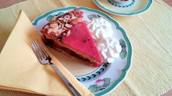 Ein St&uuml;ck gedeckter Pflaumenkuchen liegt auf einem Teller mit Sahne und einer Gabel, w&auml;hrend eine Tasse daneben steht.