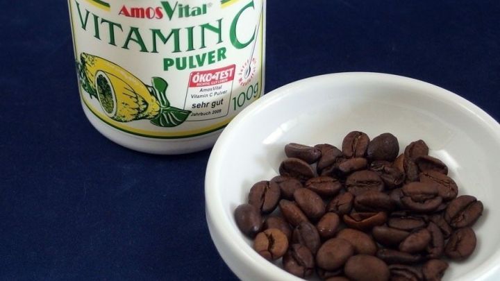 Ein kleines Sch&auml;lchen mit Kaffeebohnen steht neben einem Vitamindosenpulver, m&ouml;glicherweise zur Linderung von Kopfschmerzen.