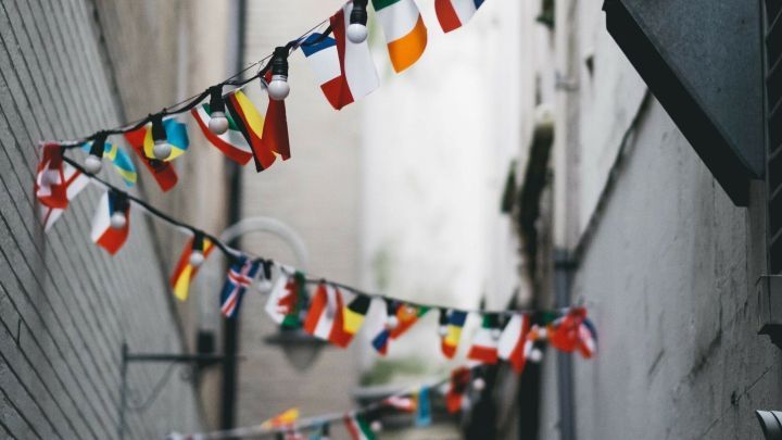 Fahnen verschiedener L&auml;nder h&auml;ngen in einer schmalen Gasse, w&auml;hrend eine Stra&szlig;enlampe das gesch&auml;ftige Umfeld beleuchtet.
