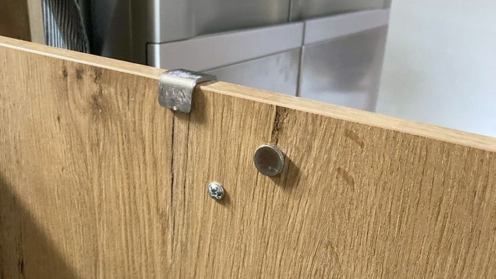 Die Schrankt&uuml;r zeigt einen defekten Verschluss, der das Schlie&szlig;en verhindert. Im Hintergrund ist eine moderne K&uuml;che sichtbar.