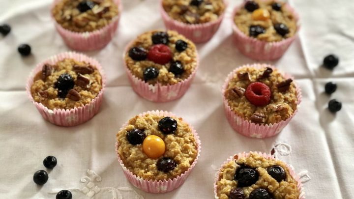 Leckere Fr&uuml;hst&uuml;cksmuffins mit Haferflocken liegen auf einem wei&szlig;en Tisch, dekoriert mit Beeren und N&uuml;ssen.