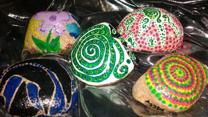 Bunte bemalte Steine liegen auf einem glitzernden Stoff, jede mit einzigartigen Mustern und Farben gestaltet.