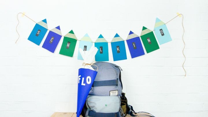 Eine bunte Girlande mit "SCHULKIND" h&auml;ngt &uuml;ber einem Rucksack und einer Schult&uuml;te, die auf einem Tisch stehen.