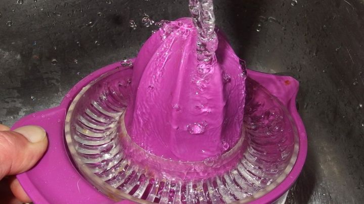 Eine lila Zitronenpresse wird unter flie&szlig;endem Wasser im Waschbecken ges&auml;ubert, um Reinheit und Frische zu gew&auml;hrleisten.