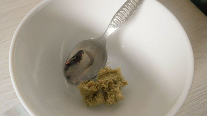 Eine silberne L&ouml;ffelruht in einer wei&szlig;en Sch&uuml;ssel, die etwas H&uuml;hnerbr&uuml;hpaste enth&auml;lt, auf einem hellen Tisch.