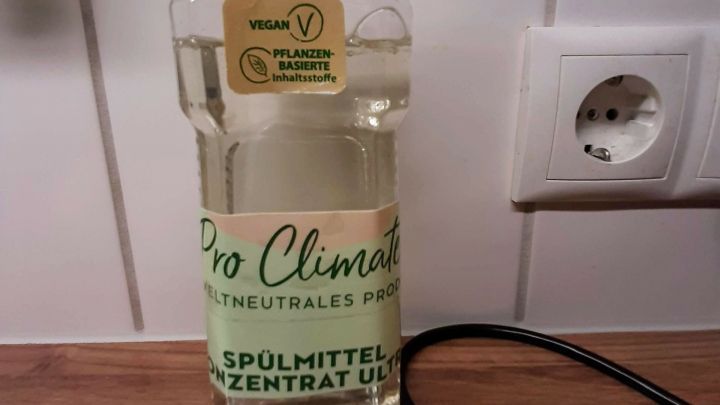Eine Flasche umweltfreundliches Sp&uuml;lmittel steht auf einer Holzoberfl&auml;che neben einem K&uuml;chensp&uuml;lbecken in einer modernen K&uuml;che.