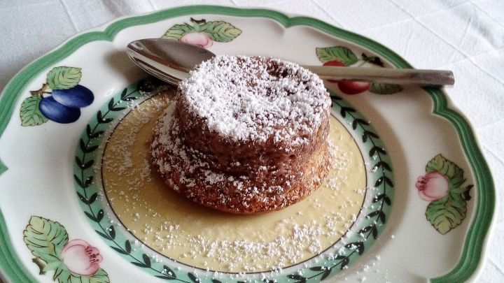 Ein Nougat-Souffl&eacute; steht auf einem dekorativen Teller, umgeben von einer feinen Sauce und mit Puderzucker best&auml;ubt.