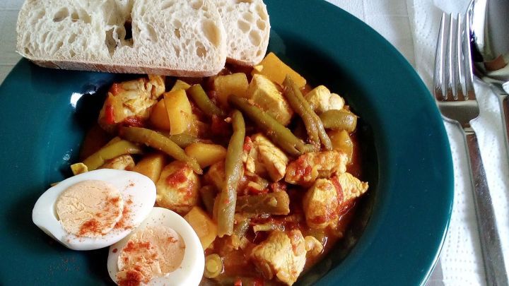 Ein gr&uuml;ner Teller mit w&uuml;rzigem H&auml;hnchen-Curry, gekochten Eiern und Brot, serviert auf einer wei&szlig;en Tischdecke.