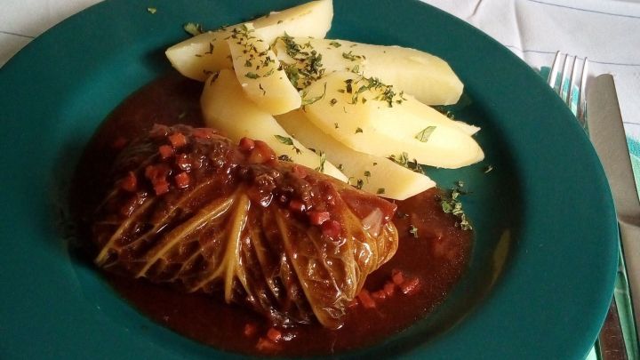 Kohlrouladen liegen in einer schmackhaften Sauce auf einem Teller, daneben liegen garnierten Kartoffelst&uuml;cke.