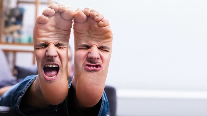 Zwei F&uuml;&szlig;e mit verzerrten Gesichtern zeigen Schmerz und Unbehagen, w&auml;hrend sie auf einem Sofa in einem hellen Raum liegen.