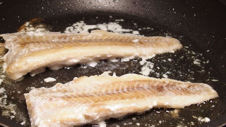 Zwei Fischfilets braten in einer beschichteten Pfanne, w&auml;hrend sich K&uuml;chenger&uuml;che im Raum verbreiten.